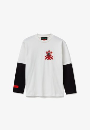 Camisa blanca de manga larga con mangas negras, gráfico pixelado de flor roja y negra en el pecho, y etiqueta roja en el puño de la manga izquierda.