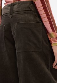 Des pantalons en velours côtelé vert foncé avec deux grandes poches arrière et une taille haute, avec des coutures visibles et une texture douce.