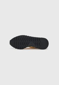 Shoe sole with black wavy tread pattern, viewed from the bottom against a plain white background.