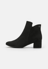 Schwarze Wildleder-Ankle Boots mit Blockabsatz, spitzer Zehenpartie und einem kleinen silbernen Logo nahe der Oberkante auf der Außenseite.