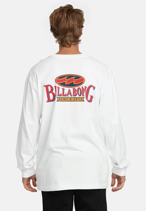 T-shirt blanc à manches longues avec un graphique rouge et bleu incluant "BILLABONG" et "SINCE 1973" au dos. Matière 100% coton, coupe décontractée.