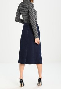 Tmavěmodrá denimová midi sukně se rovný střih, s předními švy a vysokým pasem, doplněná šedým pruhovaným rolákem a černými podpatky.