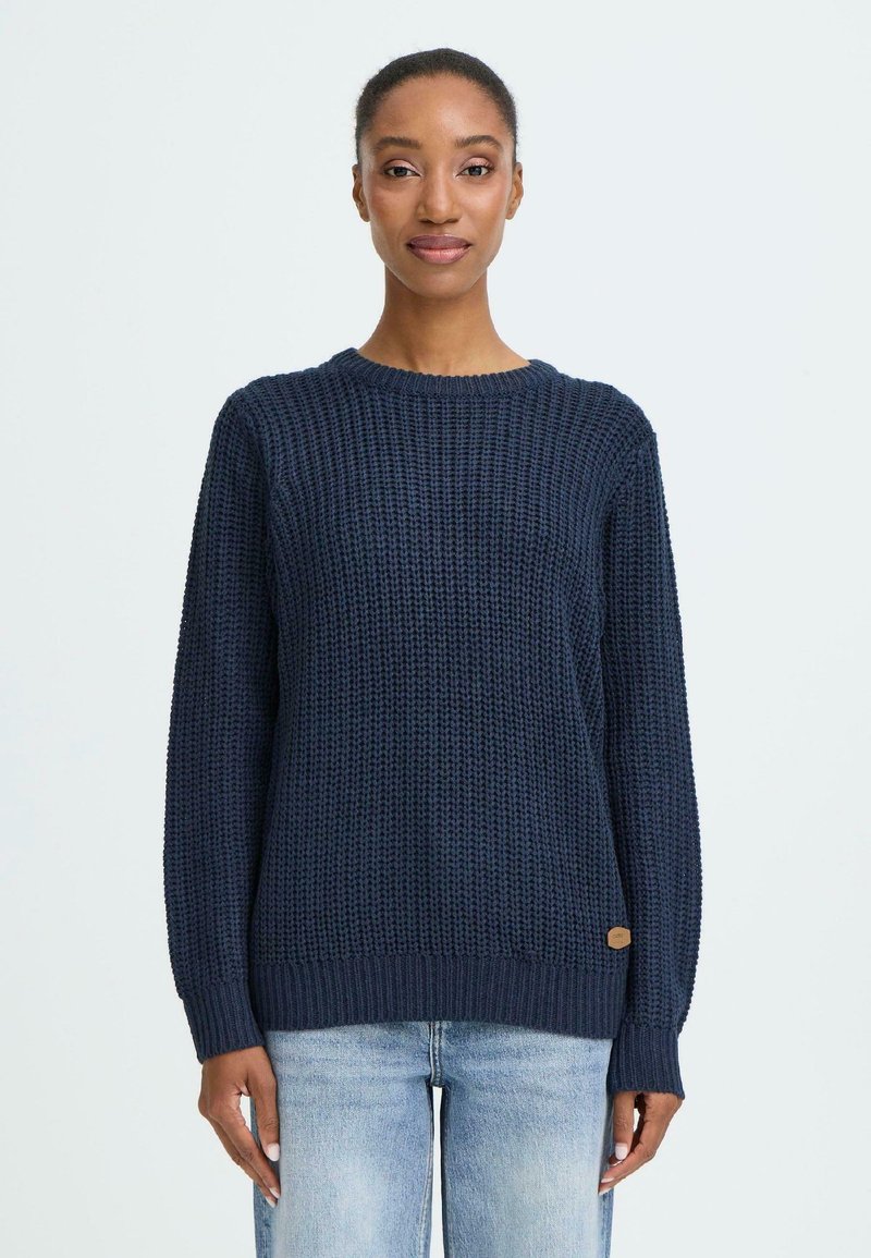 Marineblå strikket sweatshirt med et mønster, rund halsudskæring og lange ærmer. Har et lille logo-patch ved kanten.