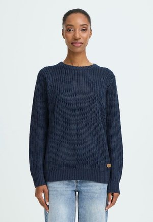 Navy blue knitted sweater with a textured pattern, round neckline, and long sleeves. Features a small logo patch on the hem.