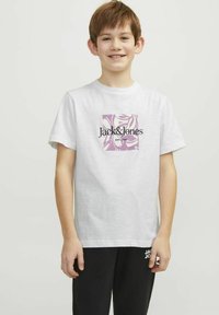 Valge puuvillane T-särk, mille esiküljel on liila graafiline disain koos tekstiga "Jack & Jones" ja "EST. 1990". Lihtne ümmargune kaelus.