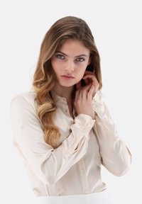 Silky cream blouse with a button-up front, long sleeves, and subtle cuff detailing. Smooth texture and fitted design.