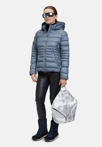 Vadderad blå jacka med huva, dragkedjefickor, svarta läderbyxor, marinblå stövlar och en silverfärgad väska med en distinkt dragkedjedesign.