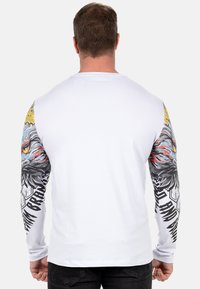 Langarm-T-Shirt aus weißer Baumwolle mit grauen Adlergraphiken auf den Ärmeln, schwarzem Text und hexagonalen Mustern.