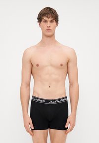 Boxer neri con tessuto morbido e cintura elastica, con il logo "JACK & JONES" in bianco. Il modello è in piedi con le braccia ai lati.