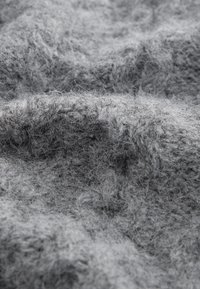 Tessuto grigio texturizzato con un aspetto morbido e soffice, caratterizzato da profondità e fibre variabili che creano un motivo superficiale irregolare.