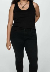 Top sin mangas negro de algodón, combinado con jeans skinny negros. Las características notables incluyen un escote redondo y un diseño sencillo.
