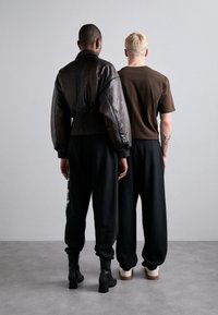 Schwarze Lederjacke im Crop-Design, braues T-Shirt, schwarze Sweatpants und kniehohe Stiefel. Minimalistisches Design, neutrale Farben, einfache Texturen.
