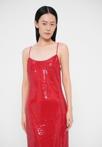 Sarkana fliteri kleita ar plānām lencītēm, veidota cieši pie ķermeņa, ar gludu tekstūru un taisnu maliņu, kas atspoguļo gaismu, piešķirot papildu mirdzumu.