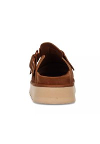 Scarpa slip-on in suede marrone con punta arrotondata, suola in gomma beige e chiusura con una sola cinghia. Texture liscia e design minimalista.