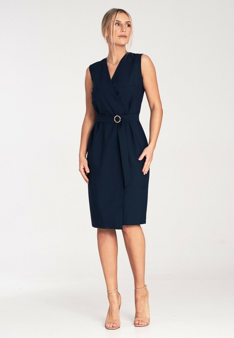 Granatowa, bezrękawnikowa sukienka kopertowa z paskiem w talii, posiadająca złotą okrągłą klamrę, do kolan, wykonana z gładkiego materiału.