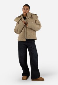 Šviesiai ruda kordūrinė striukė su dideliu apykaklės, užtrauktuku priekyje ir kišenėmis, derinama su tamsiomis džinsais ir rudos spalvos avalyne. Lygus tekstūra.