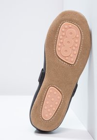 Svart skosåle med en teksturert brun semsket skinnbase og en ferskenfarget gummipute, preget med sirkulære mønstre og en hevet logo.