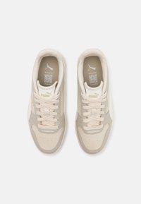 Baskets beiges avec un dessus texturé, des lacets légers et un branding subtil. Comprend des panneaux lisses et perforés pour la respirabilité.