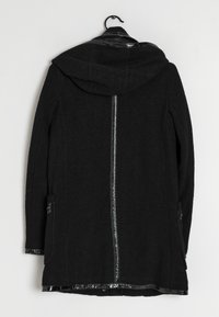 Černý kabát s kapucí, vyrobený z strukturované vlny a zdobený lesklými lakovanými koženými detaily na okrajích a zipu, se bočními kapsami.