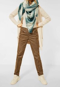 Bruna kordfläskbyxor, beige stickad cardigan, ljus topp och en rutig sjal i teal och vitt. Vita sneakers fulländar outfiten.