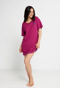 Fuchsieové tričko šaty s krátkymi rukávmi, okrúhlym výstrihom a modrým lemom na rukávoch. Vyrobené z mäkkej tkaniny, s logom na hrudi.