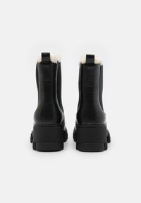Bottes noires en cuir à mi-mollet avec une semelle texturée et une douce doublure en fourrure au col. Dotées de languettes à l'avant et d'un design de talon épais.