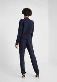 Granatowy sweter o teksturowanym wykończeniu, zestawiony z dopasowanymi spodniami wąskimi i butami na obcasie, widok z tyłu.