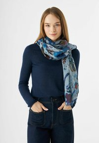 Écharpe à motifs bleus en tissu doux, drapée lâchement autour du cou, avec des motifs floraux dans des nuances de bleu et de bordeaux.