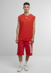 Red sleeveless t-shirt and matching shorts with white "united." text. Material appears cotton, with a relaxed fit. Paired with white sneakers.