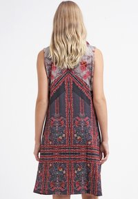 Mouwloze jurk in donkere stof met bloemenpatronen in rood en roze, met een losse pasvorm en een uitlopende zoom.