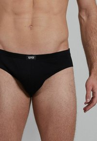 Schwarze Baumwollslips mit enganliegendem Schnitt. Verfügt über eine glatte Textur und ein Logo am Bund. Minimalistisches Design ohne zusätzliche Muster.