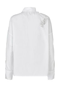 Chemise blanche à manches longues avec un pli dans le dos, ornée d'accents en dentelle sur une épaule et de fentes latérales à l'ourlet pour plus de détails.