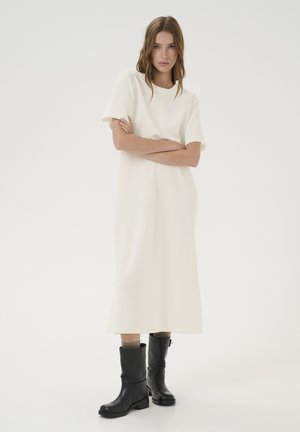Rochie albă midi cu mâneci scurte, guler rotund, textură fină; asociată cu cizme negre până la genunchi, cu toc gros și fermoar.