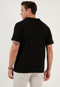 Camisa polo negra con una tela texturada, un cuello y mangas cortas. El modelo está de espaldas, revelando el diseño ajustado de la camiseta.