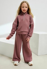 Stövt rosa träningsset som innehåller en zip-up fleecejacka med sidostrålar och vida byxor. Mjuk textur, med en avslappnad passform och avslappnad stil.