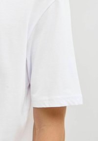 Camiseta blanca de algodón con escote redondeado y mangas cortas, de corte recto y dobladillo limpio. Textura suave con detalles mínimos de diseño.