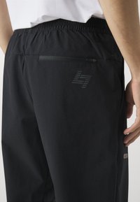 Black athletic shorts with elastic waistband, featuring a zippered pocket and a subtle logo design. Texture appears lightweight and smooth.