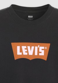 Čierne bavlnené tričko s okrúhlym výstrihom so zaujímavým veľkým oranžovým logom Levi's v kontrastnej bielej farbe, hladká textúra.