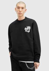 Sort sweatshirt med rund halsudskæring og lange ærmer. Har et hvidt forvrænget tekstlogo på venstre bryst. Blødt stof med en afslappet pasform.