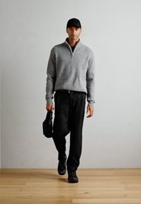 Grå strikket zip-up genser, svarte bukser, svarte sko og en svart veske. Har en tettsittende design og ribbet tekstur på genseren.