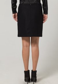 Svart ullkjol med rak skärning, som har platta fickor och en dold dragkedja baktill. Matchad med svarta anklar boots.