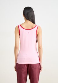 Roosa ilma varrukat top, millel on punane ääris ja Nike logo seljal. Valmistatud pehmest, venivast kangast, millel on kitsas disain ja sile tekstuur.