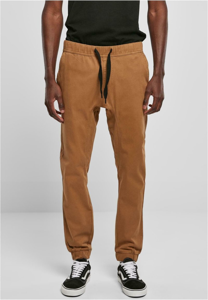 Brune joggebukser med elastisk talje og sort snor. Har tapered ankler og sidelommer, lavet af blødt stof.