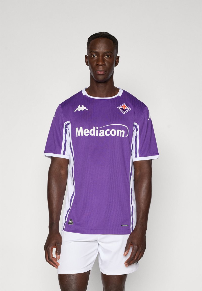 Maillot de football violet avec des accents blancs, col rond, manches courtes, arborant le logo "Mediacom" et l'emblème de l'équipe sur la poitrine. Porté avec un short blanc.