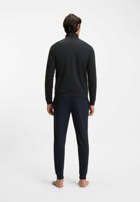 Zwarte top met lange mouwen en opstaande kraag, gecombineerd met marineblauwe joggerbroek. Glad materiaal, aansluitend ontwerp en elastische boorden.