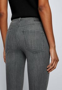 Grå jeans med en smal passform och slät yta, med två bakfickor och en liten logotyppatch vid midjan.