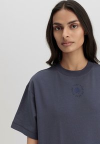 T-shirt in cotone blu navy con scollo rotondo. Presenta un logo floreale ricamato in blu sul petto. Vestibilità ampia e rilassata.