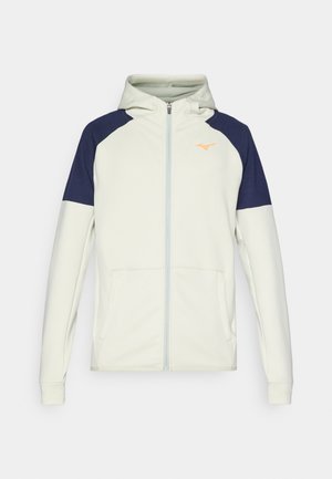 Sweatshirt com capuz e fecho éclair em creme claro, com detalhes em azul marinho nos ombros. Apresenta bolsos laterais e um logótipo laranja no peito.