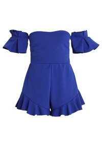 Modrý overal bez ramínek vyrobený z texturované látky, s objemovými rukávy a volánkem na šortkách.