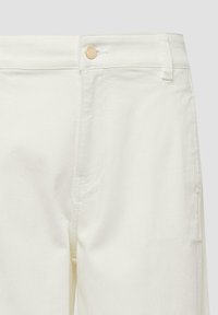Gros plan sur un jean en denim blanc montrant un bouton doré, une boucle de ceinture, une poche avant et des détails de couture.